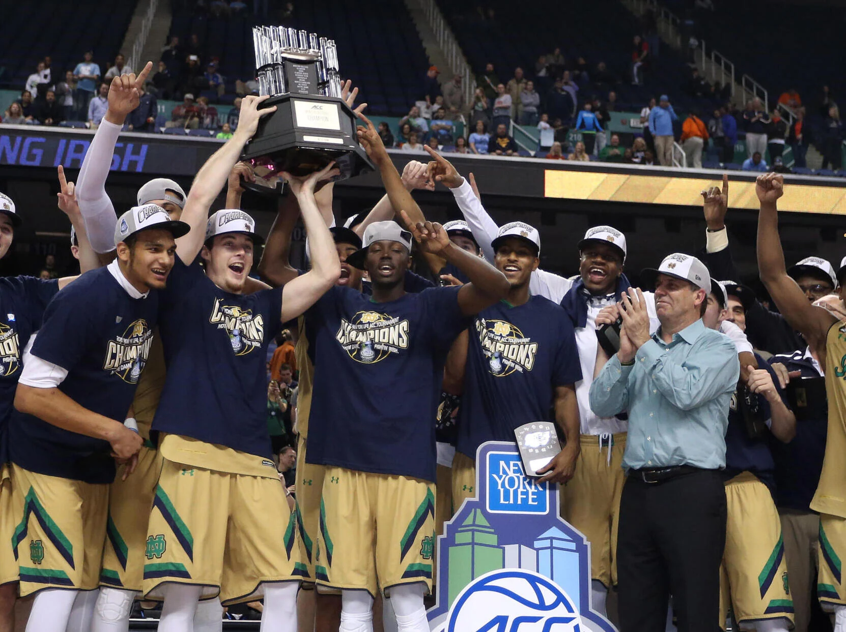 Notre Dame players lift the ACC trophy in championship shirts and caps