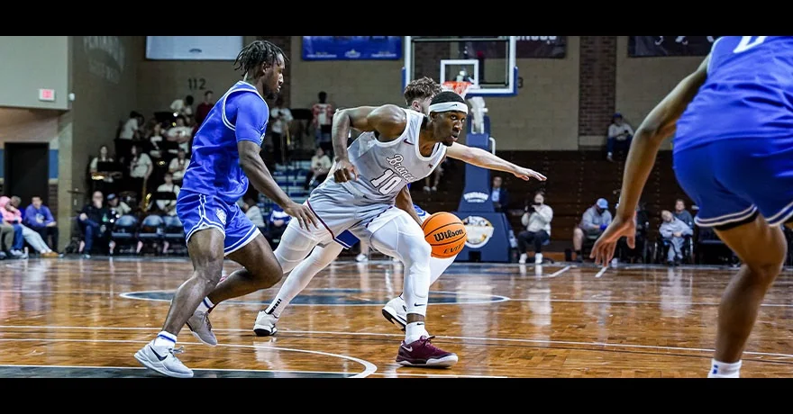 A player in white driving between blue defenders during an earlier Sanford Pentagon basketball game