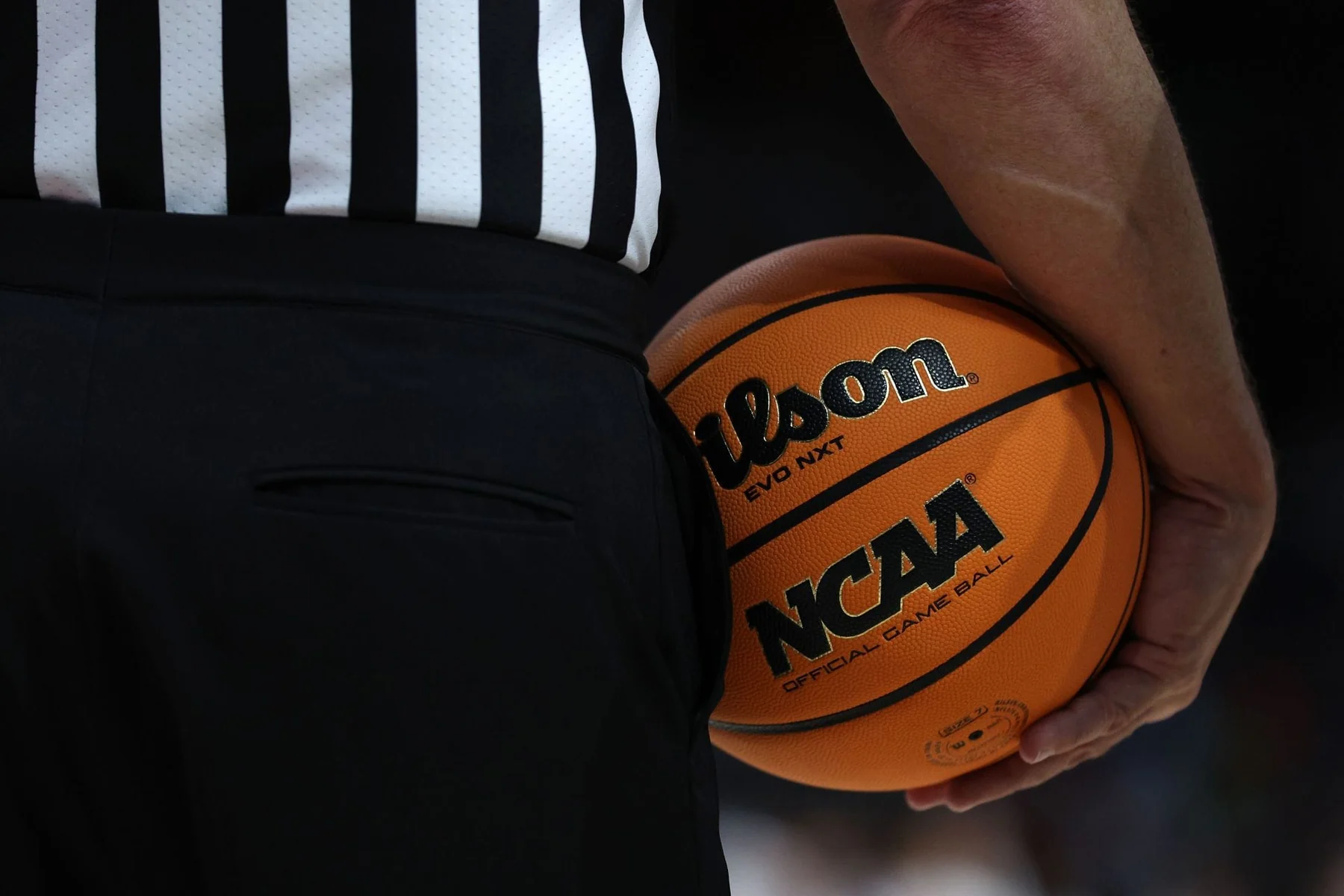 A referee holds an orange Wilson EVO NXT basketball beside a black-and-white striped shirt