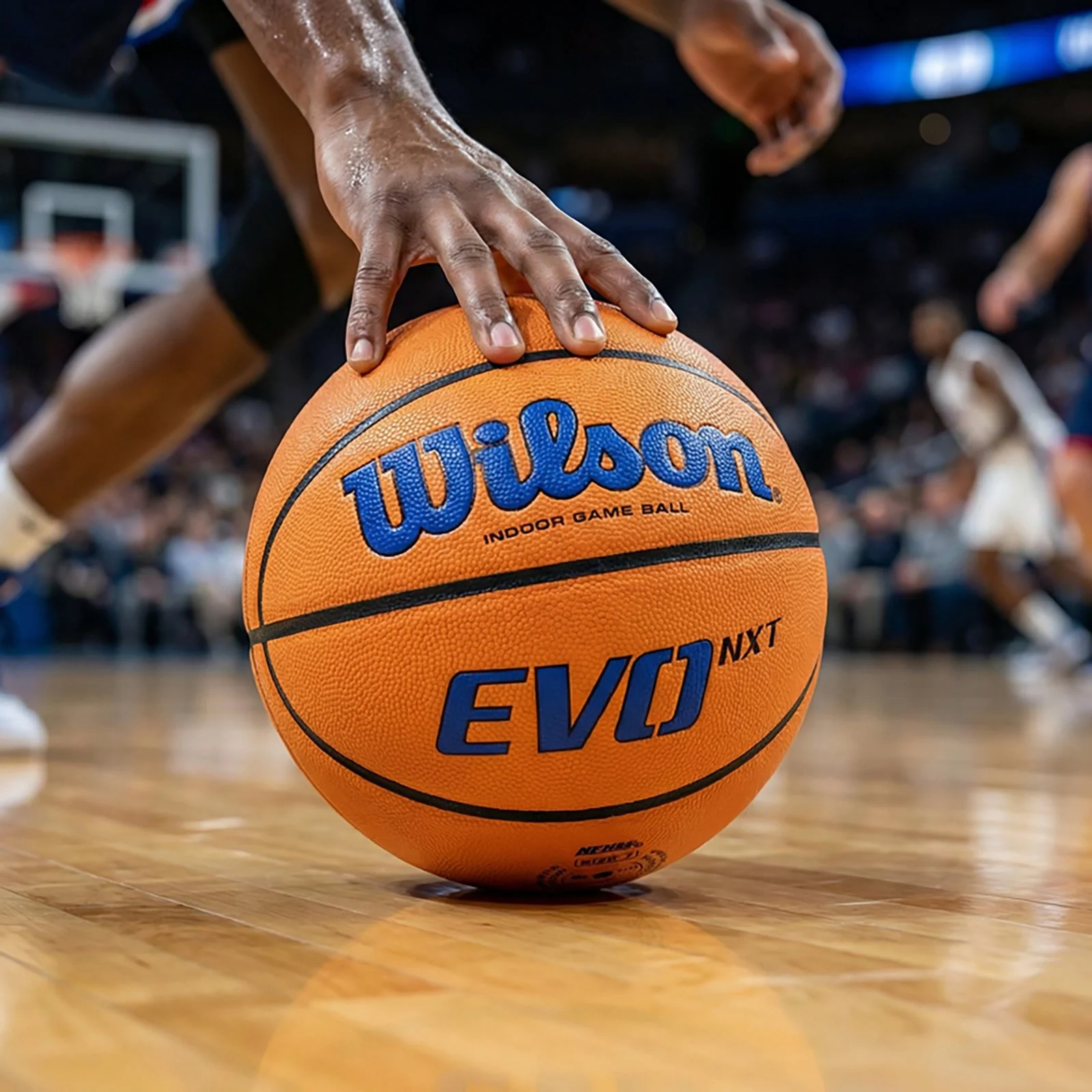 A player's hand controls an orange Wilson EVO NXT basketball with blue lettering on a wooden court