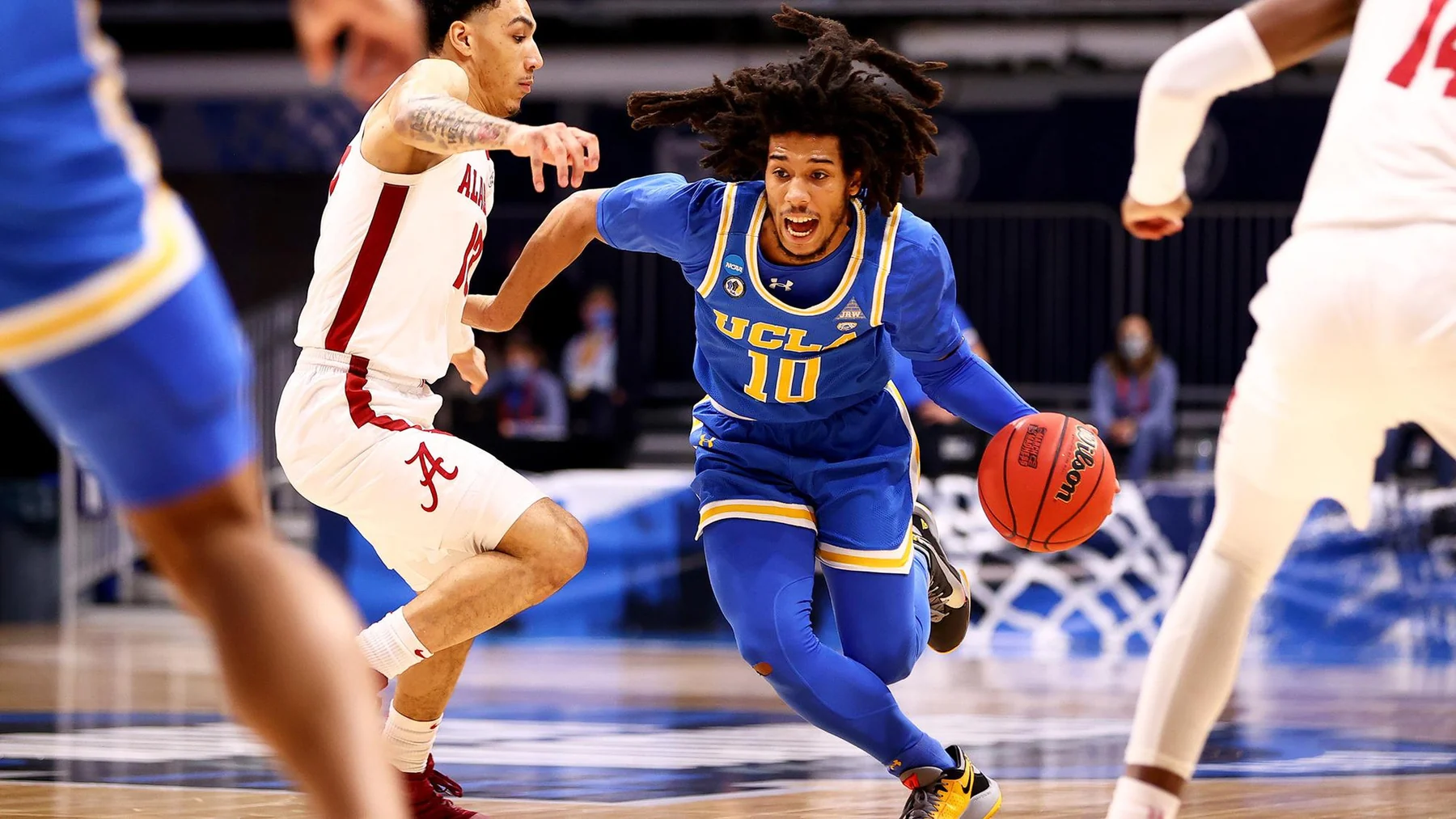 A UCLA player in a blue uniform driving with the ball between Alabama defenders