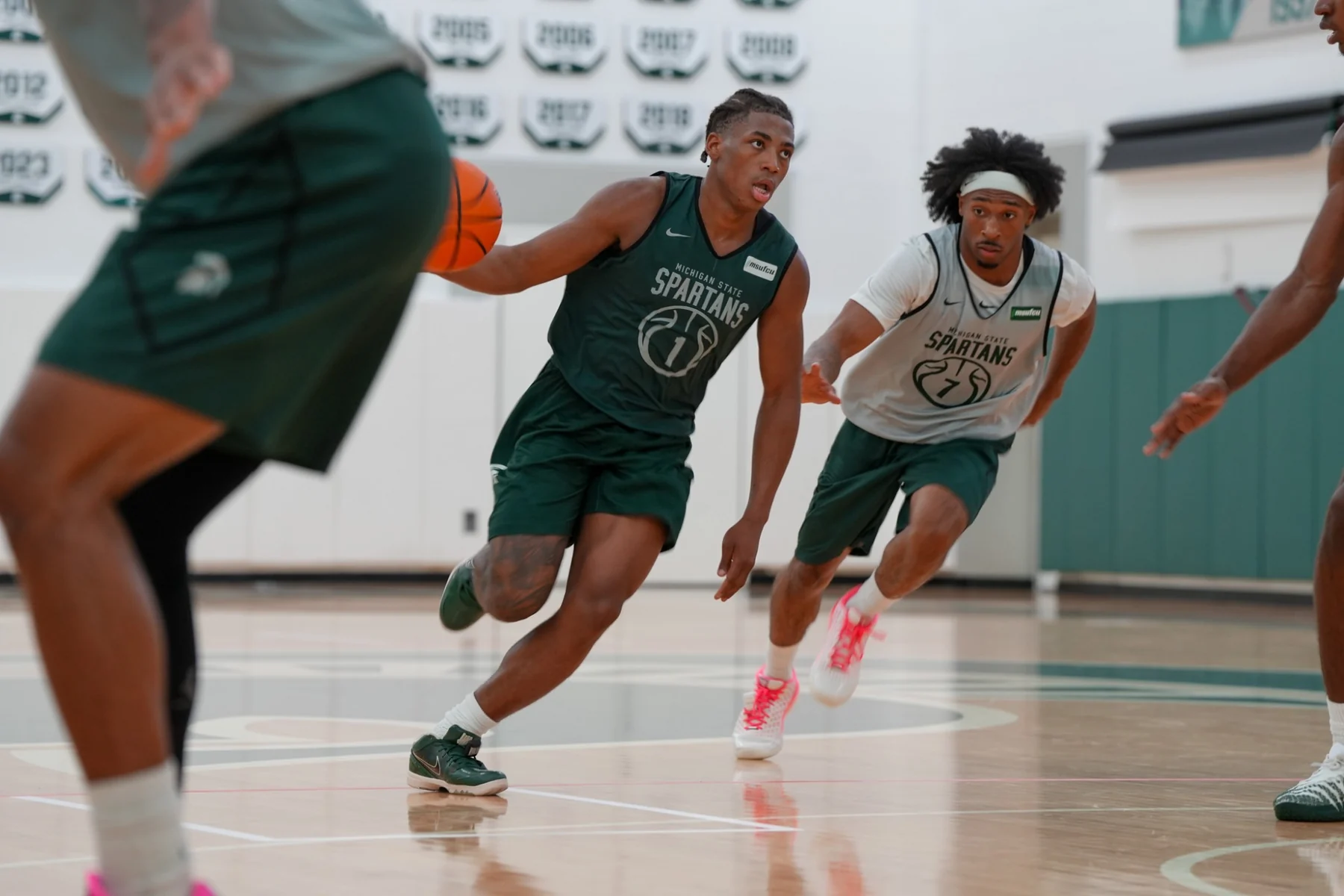 Michigan State ballhandler in a green practice jersey moves past teammates in a gym