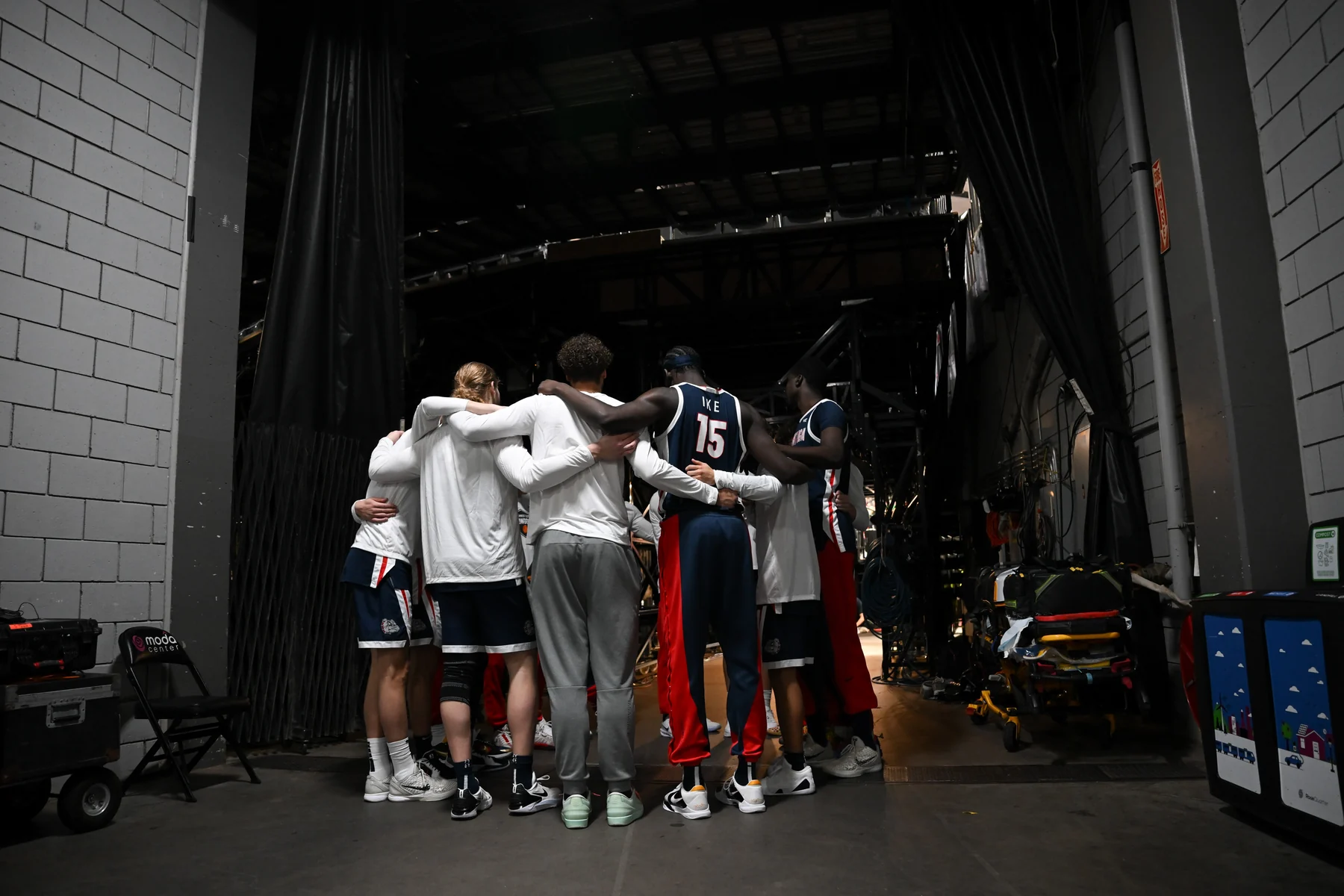 Gonzaga players gather with arms around one another in an arena tunnel