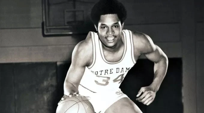 Austin Carr wears a Notre Dame number 34 uniform in a low dribbling stance with a basketball in a gym