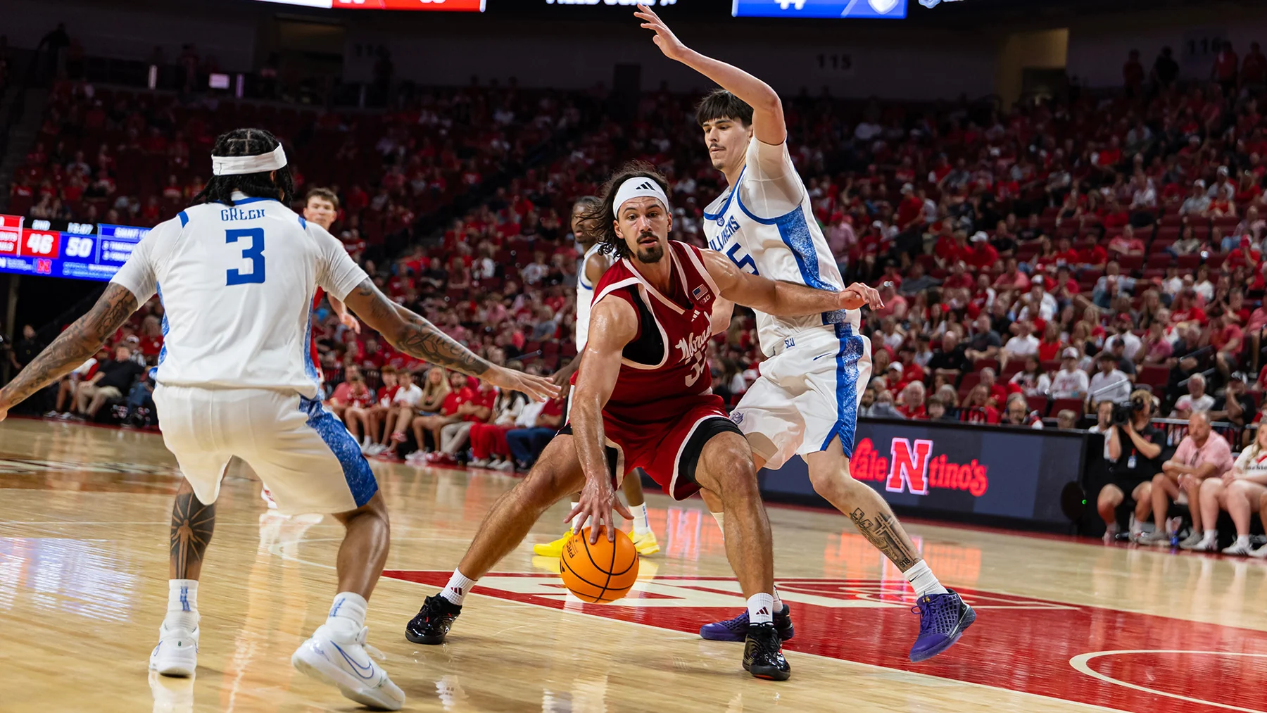 Nebraska player in red number 31 dribbles between two Saint Louis defenders in white and blue