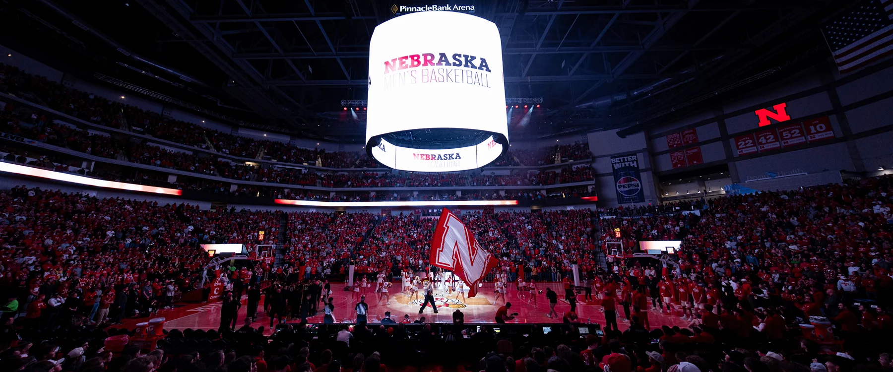 Pinnacle Bank Arena basketball floor beneath a center-hung Nebraska display with an N flag and red-clad crowd