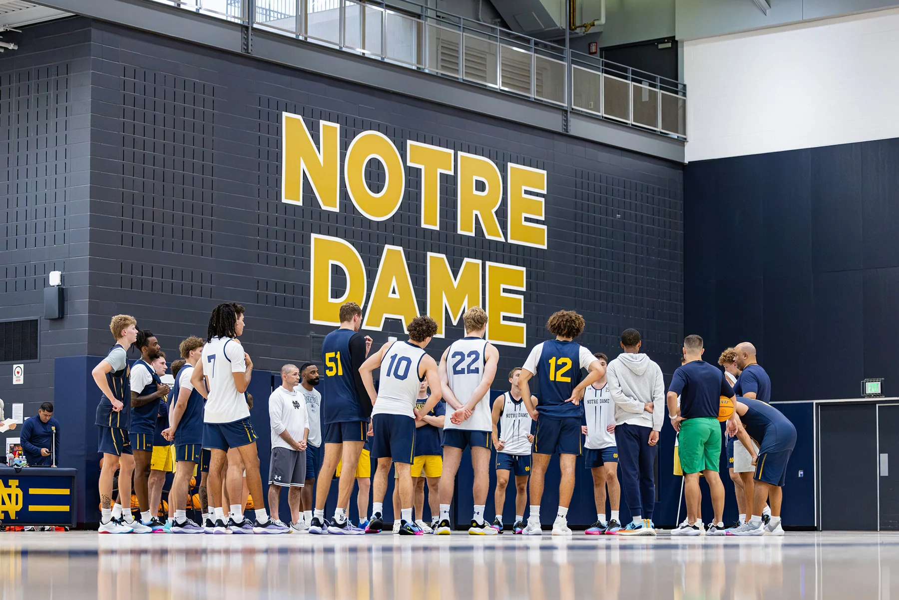 Notre Dame players and coaches gathered on a practice court beneath the school name