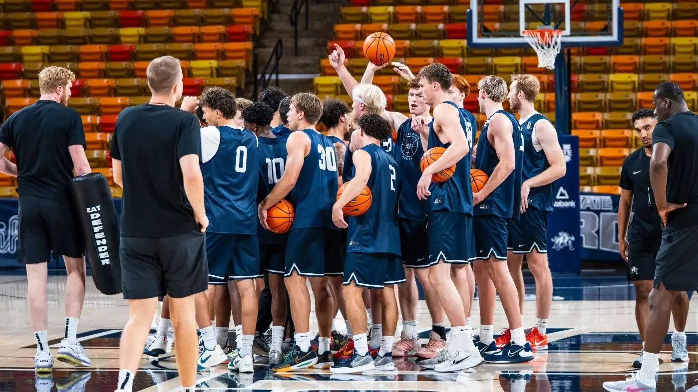 Utah State players and coaches gather in a practice huddle holding basketballs