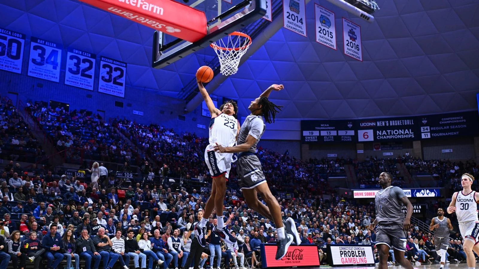 UConn player goes toward the basket against a defender in a packed home arena
