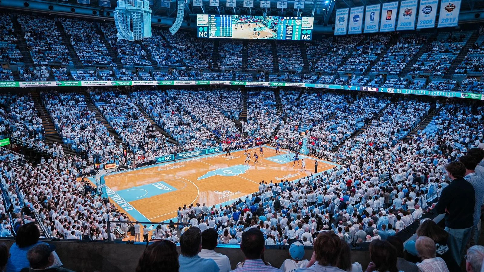 Wide view of the Smith Center basketball court surrounded by a light-blue and white crowd with banners overhead