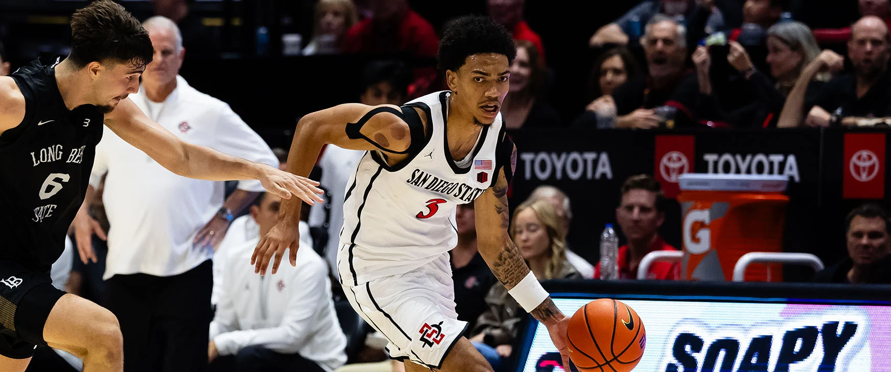 San Diego State player in white number three dribbles beside a Long Beach State defender in black