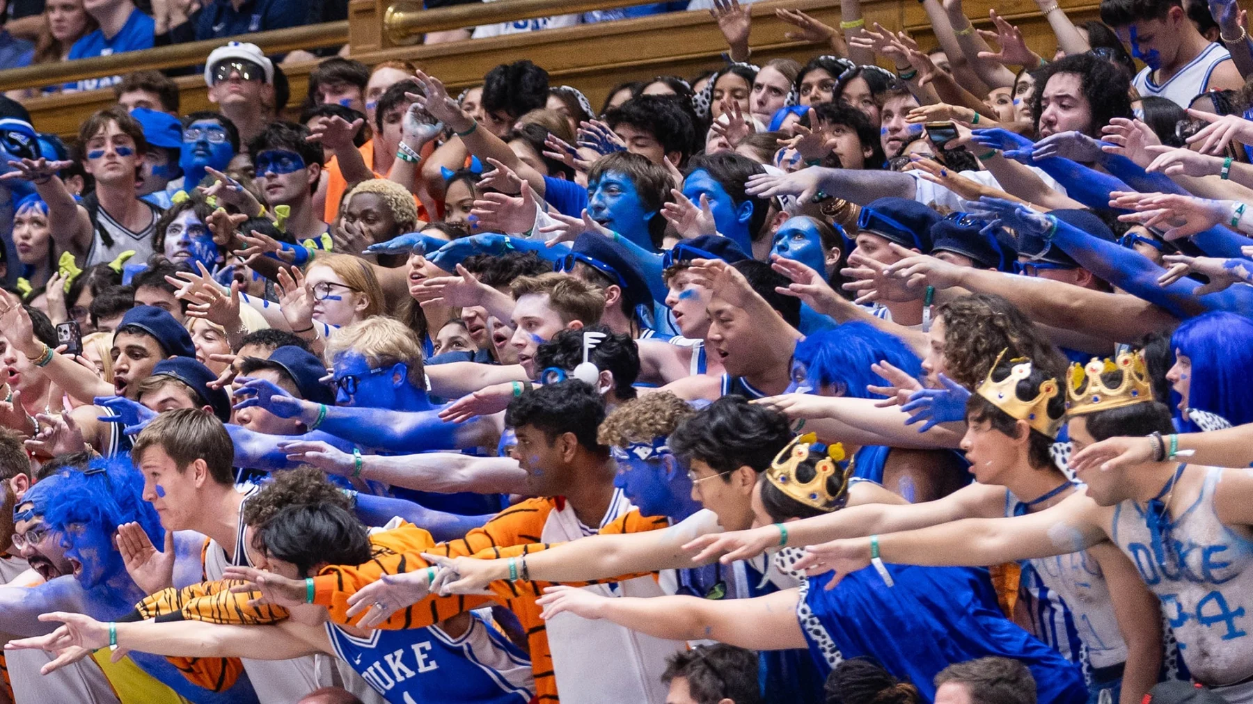 Fans in Duke jerseys with blue-painted faces reach toward the court from crowded stands
